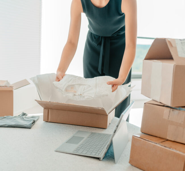 Small business entrepreneur woman unpacking dress clothes returned in mailing box for shipping from online store.